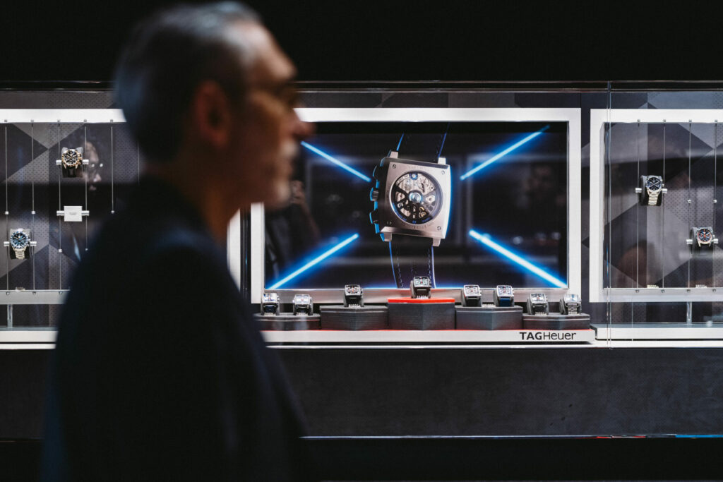 Homme de profil en premier plan et en arrière plan une vitrine de montre de luxe.