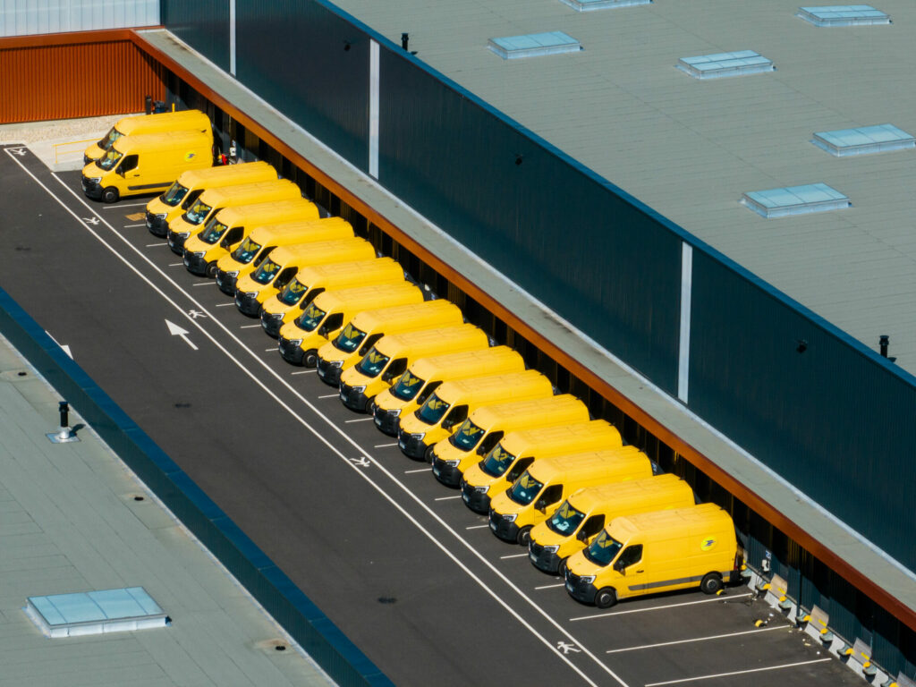Photo de drone d'une rangée de véhicules La Poste jaune devant une base logistique.