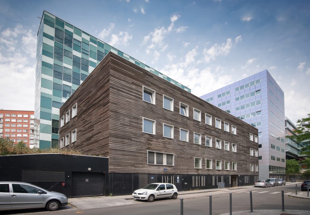 Un bâtiment rectangle situé en ville avec à l'arrière des buildings.