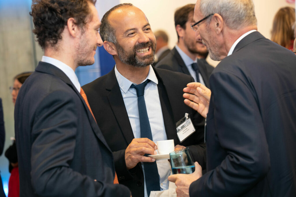 3 hommes souriants, discutent avec un verre à la main pendant la plénière AXA.