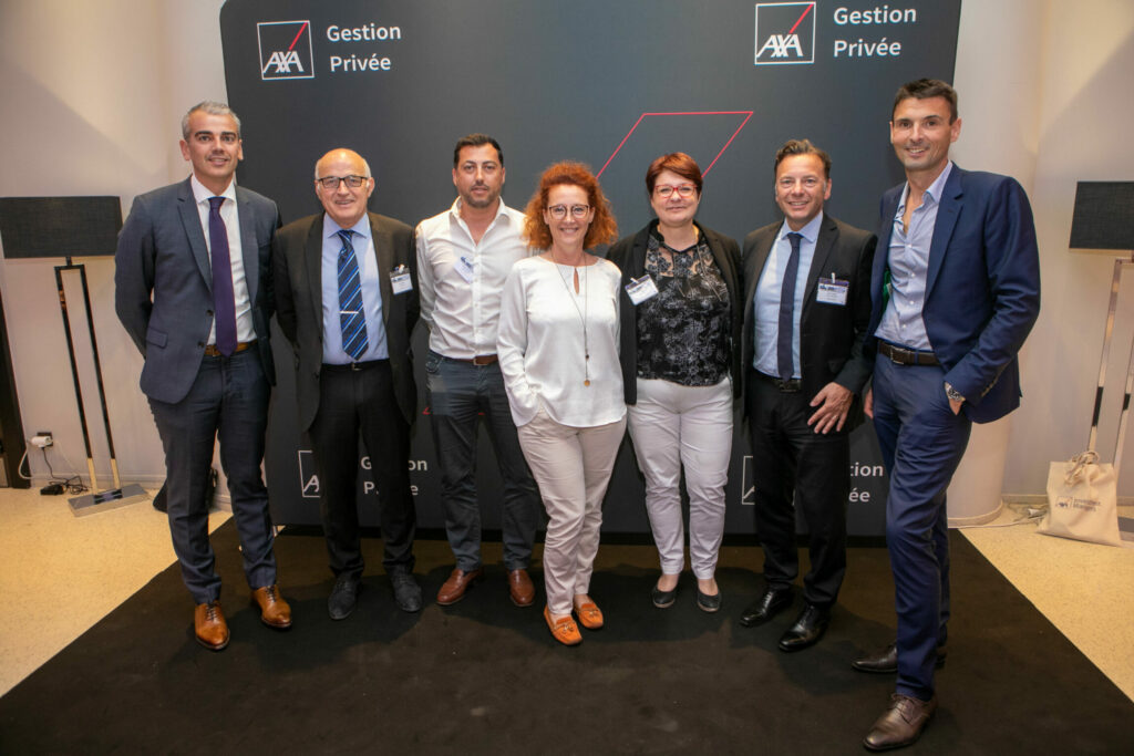 Un groupe de 7 personnes se tiennent personnes souriantes se tiennent devant un photo-call personnalisé AXA.