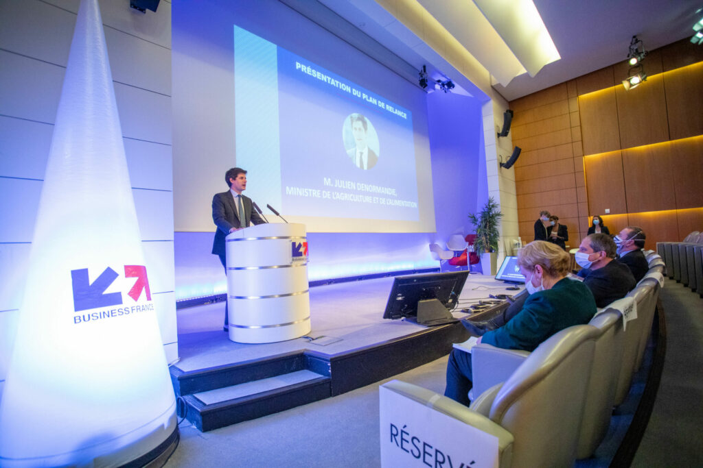 un homme se tient debout sur scène, à l'occasion d'une conférence business france. Le logo business est en premier plan.