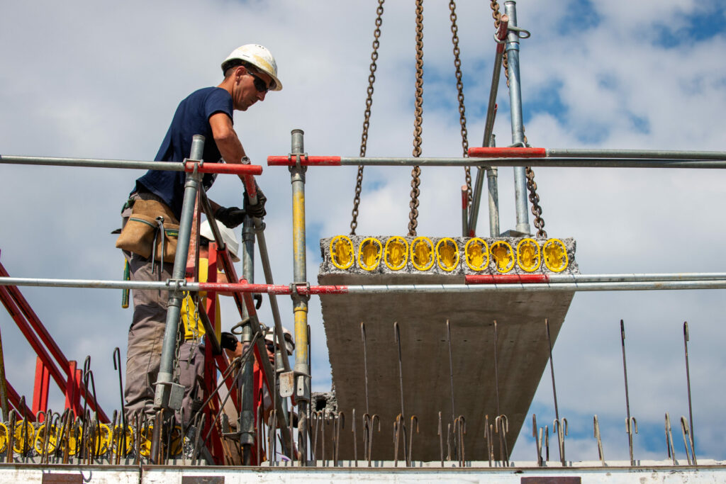 Un homme sur un chantier qui guide un grutier pour le bon placement d'une plaque de béton