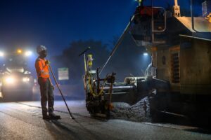 Un homme avec un râteau prêt a appliquer du béton sur une route pendant un chantier de nuit.