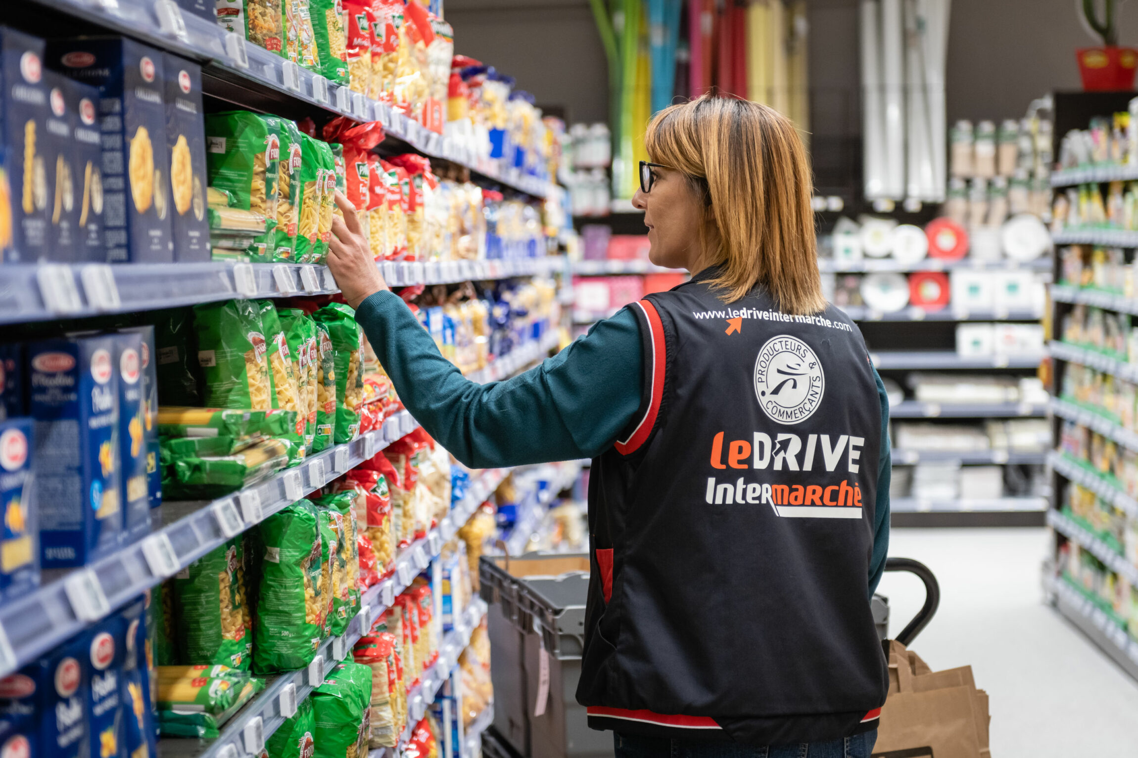 Une femme fait de la mise en rayon dans un supermarché. Elle se trouve dans un rayon de pâtes.