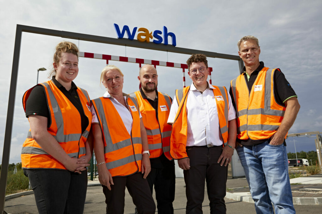 Portrait de groupe de 5 collaborateurs devant le portique d'une station de lavage Total.